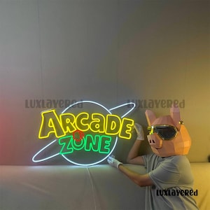 May include: A neon sign with the words "Arcade Zone" in yellow and green, surrounded by a white outline of a planet. A person wearing a pig-shaped mask with gold-rimmed glasses is holding the sign.