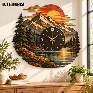 May include: A circular wall clock featuring a layered wood landscape scene with snow-capped mountains, a forest of pine trees, a lake, and a large orange sun. The clock face is black with gold hands and numerals 3, 6, 9, and 12.