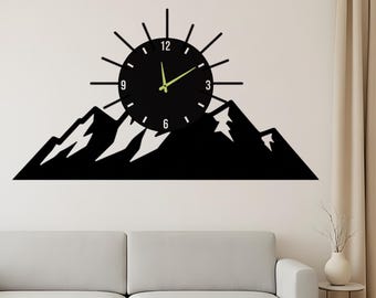 May include: Black wall clock with a mountain silhouette design. The clock face is round with a sunburst design around it. The clock hands are a bright green color. The clock is mounted on a white wall above a white sofa.
