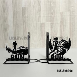May include: Black metal bookends with a running figure silhouette and mountain scenery. The word "RUN" is at the base of each bookend. These bookends are designed to keep books upright and organised on a shelf.