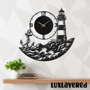 Puede incluir: Reloj de pared de metal negro con diseño de faro, ancla y olas. La esfera del reloj es negra con manecillas y números dorados. El faro tiene rayas blancas y negras. El reloj está montado en una pared blanca.