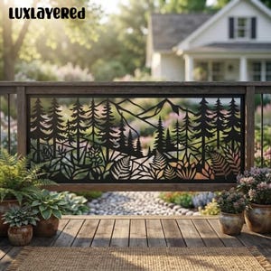 May include: A black metal railing panel featuring a laser-cut design of a dense forest with tall pine trees, mountain silhouettes, and various ferns. The rectangular panel is mounted between wooden posts on a deck overlooking a garden.