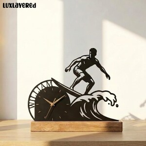 May include: A black metal desk clock featuring a silhouette of a surfer riding a wave. The clock face is integrated into the wave design and includes the name WILLIAM in capital letters along the left edge. The clock rests on a rectangular wooden base.