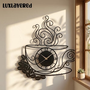 May include: A black metal wall clock shaped like a coffee cup with swirling steam patterns rising from the top. The clock face is circular with gold hands and numbers 3, 6, 9, and 12. A cluster of coffee beans is attached to the lower left side.