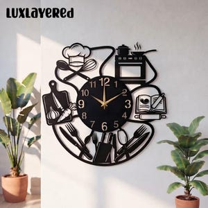 May include: A black wall clock featuring a central circular face with gold hands and numbers. The frame is decorated with kitchen-themed silhouettes including a chef hat, stove, cutting board with garlic and carrot, and various utensils.