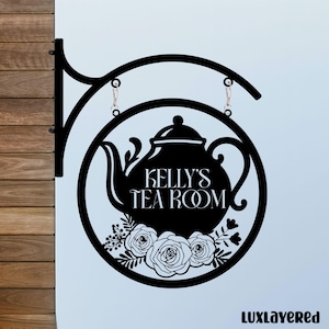 May include: Black metal sign for "Kelly's Tea Room" featuring a teapot design within a circular frame. The sign displays the text "Kelly's Tea Room" and floral details. It is suspended from a decorative bracket.