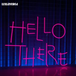 Puede incluir: Letrero de neón rosa que dice "HELLO THERE" sobre un fondo de rejilla azul. El texto está iluminado en un color rosa brillante. La palabra "LUXLAYERED" está en la esquina superior izquierda.