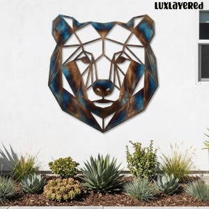 Könnte beinhalten: Ein geometrisches Wandkunstobjekt aus Metall in Form eines Bärenkopfes mit einem facettierten Design und einem metallischen Finish in Bronze-, Kupfer- und Blautönen. Der Text "LUXLAYERED" ist in der oberen rechten Ecke des Bildes aufgedruckt.