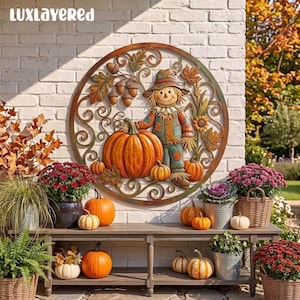 May include: A circular metal wall art piece featuring a scarecrow, a large orange pumpkin, acorns, and autumn leaves. The design is framed by decorative scrollwork. The text "LUXLAYERED" is visible in the upper left corner of the image.