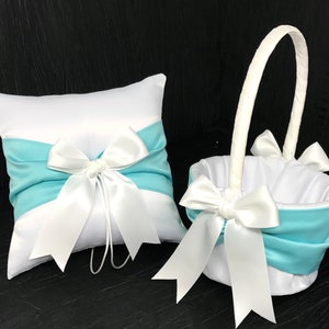 May include: A white satin pillow with a light blue satin bow and a white satin basket with a light blue satin bow. Both items are for a wedding ceremony.