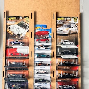 May include: A wooden display shelf featuring Hot Wheels cars, with the "Formula 1" and "Hot Wheels" logos at the top. The shelf holds various miniature race cars in their original packaging, including models from Porsche, McLaren, and other brands.