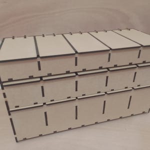 May include: A three-tiered, light brown wooden storage box with multiple compartments. Each tier has individual pull-out drawers. The box is constructed from laser-cut wood, with visible slots and a clean, geometric design. The box is suitable for organizing small items.