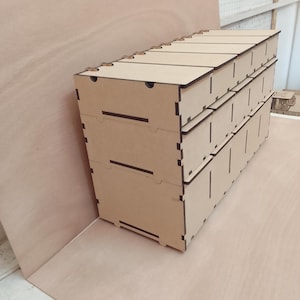 May include: A stack of three-drawer wooden storage boxes. The boxes are made of light brown wood with dark brown edges and are assembled with interlocking joints. The top of the boxes have small finger holes for easy opening.