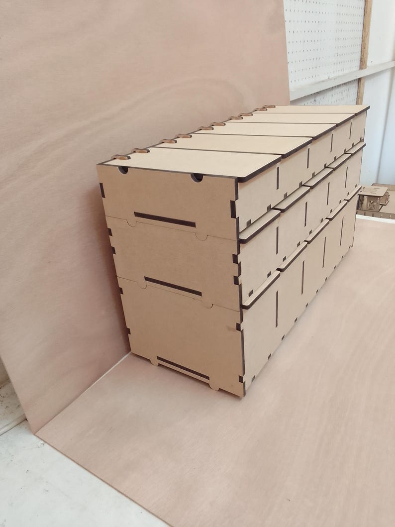 May include: A stack of three-drawer wooden storage boxes. The boxes are made of light brown wood with dark brown edges and are assembled with interlocking joints. The top of the boxes have small finger holes for easy opening.