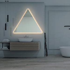May include: A modern bathroom featuring a triangular mirror with an illuminated edge, a white porcelain sink with chrome taps, a wooden vanity with two drawers, and a white bathtub.