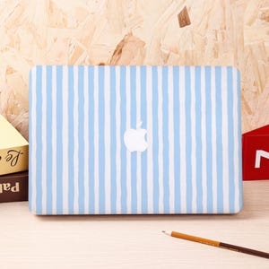 Może przedstawiać: Etui na laptopa w biało-błękitne pionowe paski z logo Apple. Obudowa jest prostokątna. Tło to wzór jasnego usłojenia drewna.