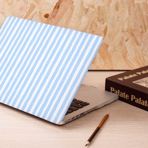 Może przedstawiać: Laptop z jasnoniebiesko-białą obudową w paski. Obok laptopa znajduje się brązowa książka z napisem "Palate Palate". Na stole leży brązowo-beżowy oł&oacute;wek.