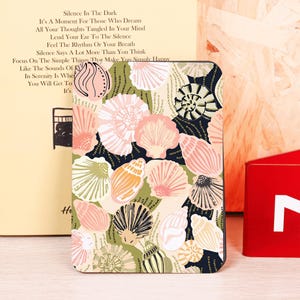 May include: A decorative notebook featuring a seashell pattern in shades of pink, beige, and green on a dark blue background. The notebook is rectangular and has rounded corners. Text on the left side reads "Silence In The Dark".
