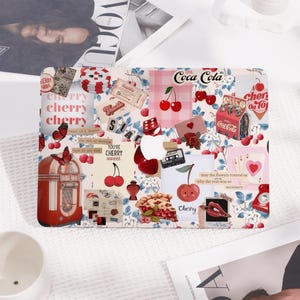 Op de afbeelding: Een laptop skin met een collage van afbeeldingen, waaronder kersen, een jukebox, een blikje Coca-Cola en de tekst "Coca-Cola" en "Cherry".