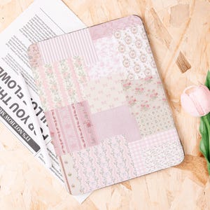 Może przedstawiać: Prostokątny, różowy wzór patchworkowy z różnymi wzorami kwiatowymi, w paski i kokardki. Wzór znajduje się na metalowej powierzchni. Różowy tulipan jest w tle. Wzór patchworkowy to mieszanka jasnych i ciemnych odcieni różu.