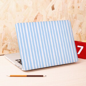Może przedstawiać: Laptop z jasnoniebiesko-białą obudową w paski. Laptop jest otwarty na jasnej drewnianej powierzchni, z oł&oacute;wkiem i czerwonym blokiem z numerem 7.