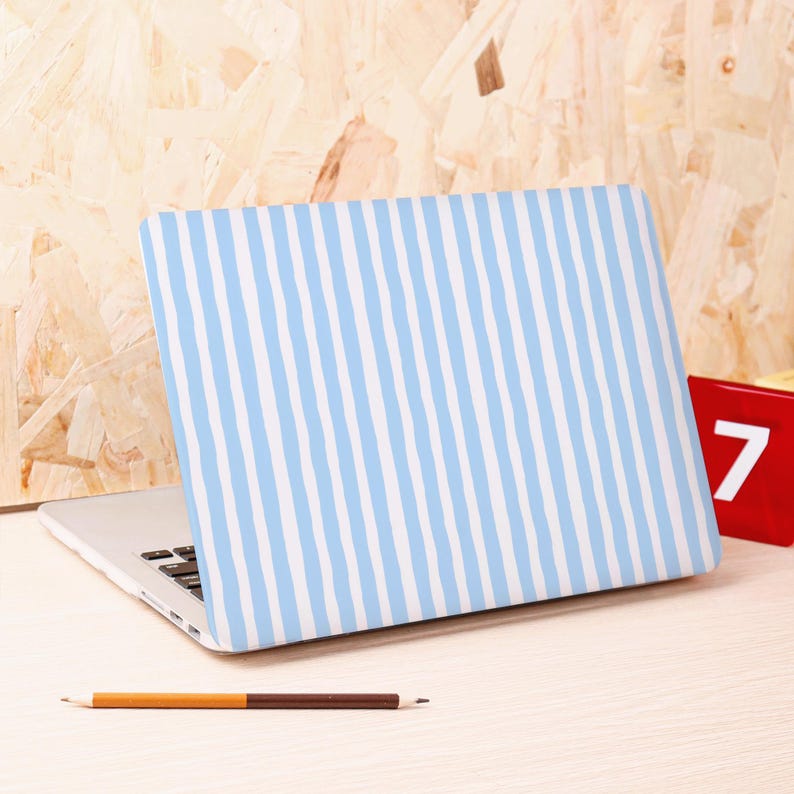 Może przedstawiać: Laptop z jasnoniebiesko-białą obudową w paski. Laptop jest otwarty na jasnej drewnianej powierzchni, z oł&oacute;wkiem i czerwonym blokiem z numerem 7.