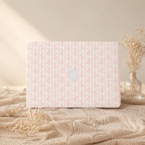 May include: A laptop skin featuring a repeating pattern of vertical light pink stripes alternating with thin white stripes decorated with small pink flowers and green leaves. The skin is applied to a laptop with a centered silver Apple logo.