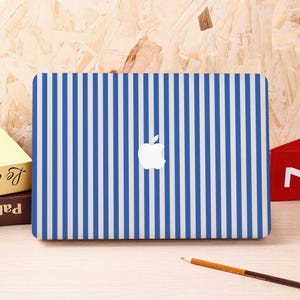 May include: A blue and white striped laptop cover with the Apple logo in the center. The cover is rectangular and has vertical stripes. The background is a light brown wood.