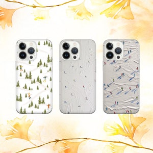 May include: Three white iPhone cases with different designs. The first case has a white background with a pattern of green trees and skiers. The second case has a white background with a pattern of white lines and skiers. The third case has a white background with a pattern of skiers on a white surface.