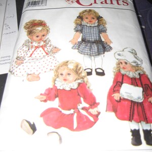 May include: A Simplicity Crafts sewing pattern for making dolls. The pattern includes four different doll outfits, including a plaid dress, a red dress with a white sash, a white dress with red hearts, and a red dress with a white bag. The pattern number is 9478.
