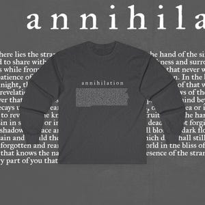 May include: Dark gray long-sleeve shirt with the word "annihilation" printed in white, along with a block of text. The shirt is a solid color and has a crew neck.
