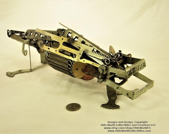 May include: A steampunk-style metal sculpture of a dragon, made from repurposed clock parts and other metal pieces. The dragon is in a crouching position with its wings spread out. The sculpture is painted in shades of gold, silver, and black.