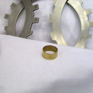 May include: A gold-colored metal ring sits on a white fabric surface. Two silver metal gears are in the background.