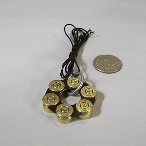 May include: A necklace made from a circle of six bullet casings with a brown leather cord. The casings are gold colored and have the words "CHESTER" and "WIN" on them.