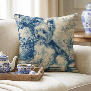 May include: A square throw pillow featuring a blue and white toile-style print of a Yorkshire Terrier dog surrounded by floral patterns. The design is rendered in shades of blue on a light, textured fabric background, creating a detailed illustration.