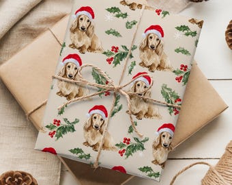 May include: Wrapped gift with festive wrapping paper featuring dachshunds wearing Santa hats, holly, and berries. The package is tied with twine and rests on a neutral surface, with pine cones and twine spools in the background.