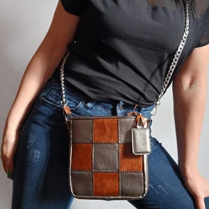 Può includere: Una borsa a tracolla patchwork con una catena d'argento. La borsa presenta un motivo a scacchiera di quadrati di pelle marrone, bronzo e color rame. Un piccolo ciondolo rettangolare argentato pende dalla borsa.