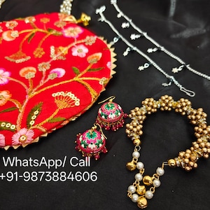 May include: A red embroidered clutch with floral patterns, paired with matching earrings and a gold beaded bracelet. Also included are silver chain hair accessories. The jewelry set is displayed on a black surface.