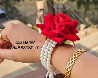 May include: A red rose corsage with white pearl strands and gold accents. The corsage is attached to a wrist with a gold bracelet. The image also contains the text "qqs2tsdW 208488828e-te+".