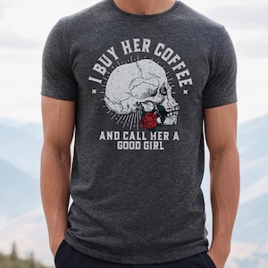 May include: Dark gray t-shirt featuring a skull graphic with a red rose and the text "I BUY HER COFFEE AND CALL HER A GOOD GIRL" in white. The shirt is made of a soft material and has short sleeves.