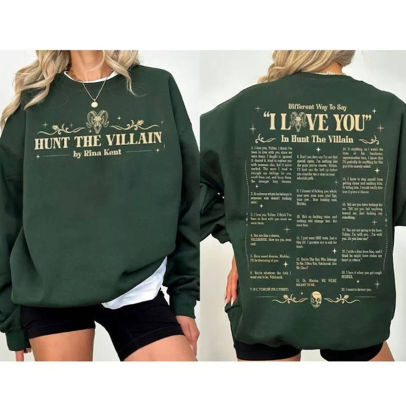 May include: A dark green sweatshirt featuring the text "HUNT THE VILLAIN by Rina Kent" on the front. The back of the sweatshirt displays the text "Different Way To Say 'I LOVE YOU' In Hunt The Villain".