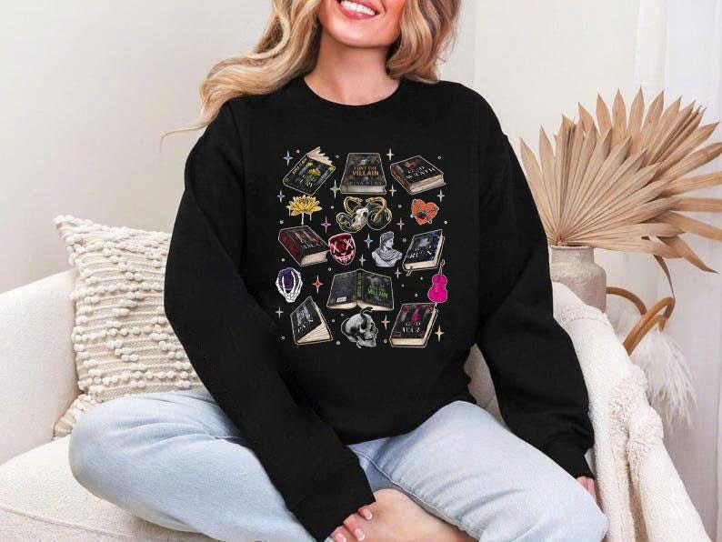 May include: Black sweatshirt featuring a collection of illustrated books, a skull, a flower, a gemstone, a bust, a guitar, and other fantasy-themed elements. The design includes various colors and details, creating a whimsical and artistic aesthetic. The sweatshirt is a casual garment.