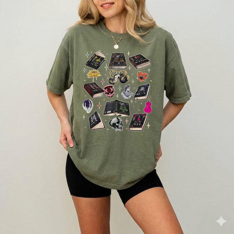 May include: Olive green t-shirt featuring a collection of illustrated books, a skull, a flower, and other graphics. The design includes a variety of colors and shapes, creating a unique and artistic aesthetic. The shirt is a comfortable, casual style.