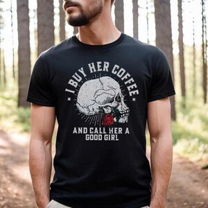 May include: Black t-shirt with a graphic of a skull and a red rose. The text on the shirt reads "I BUY HER COFFEE AND CALL HER A GOOD GIRL". The shirt is short-sleeved and has a crew neck.