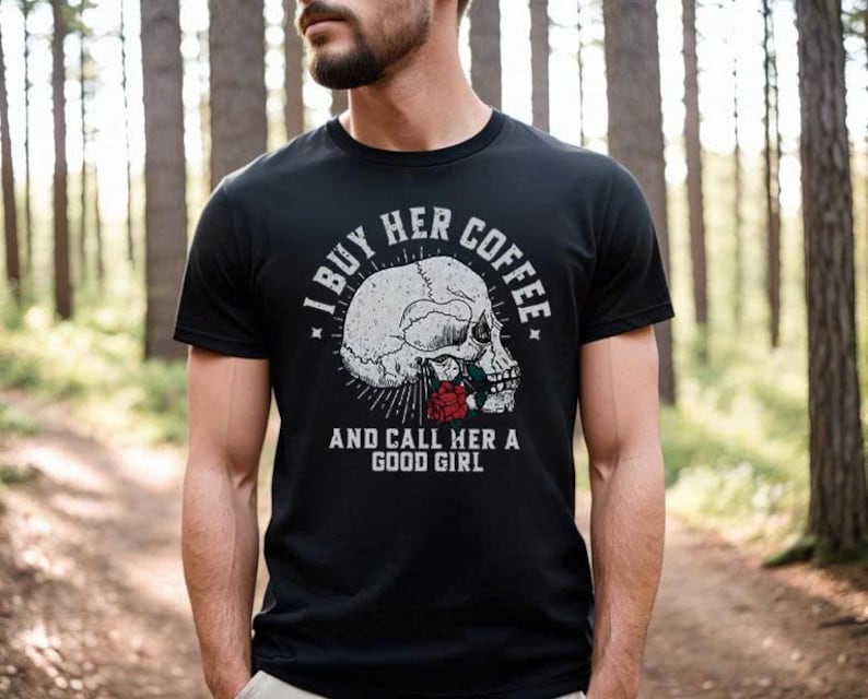 May include: Black t-shirt with a graphic of a skull and a red rose. The text on the shirt reads "I BUY HER COFFEE AND CALL HER A GOOD GIRL". The shirt is short-sleeved and has a crew neck.