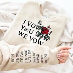 May include: Cream-colored sweatshirt with the text "I VOW YOU VOW WE VOW" and a red rose graphic with butterflies. The sleeve displays the words "LITTLE ONE, LITTLE ANGEL, LITTLE DEMON, LITTLE DARLING, SWEET CHEEKS, SWEETHEART, BABY GIRL, PRINCESS, DOLL FACE."