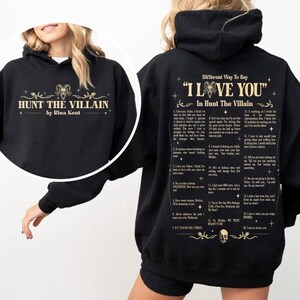 May include: Black hoodie featuring the text "HUNT THE VILLAIN" and "by Rina Kent" in gold lettering on the front. The back of the hoodie displays a list of phrases under the title "Different Way To Say 'I LOVE YOU' In Hunt The Villain."