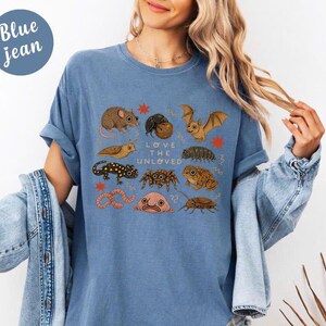 May include: Blue jean colored t-shirt with a graphic of various insects and small animals, including a bat, spider, and worm. The text "Love the Unloved" is printed in the center of the design.