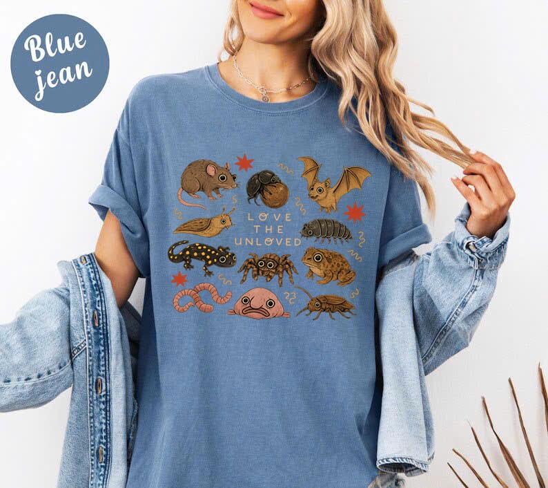 May include: Blue jean colored t-shirt with a graphic of various insects and small animals, including a bat, spider, and worm. The text "Love the Unloved" is printed in the center of the design.