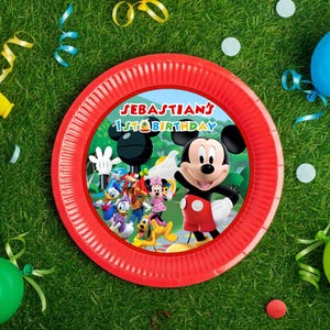 Puede incluir: Un plato de papel rojo con Mickey Mouse y sus amigos, con el texto "Sebastian's 1st Birthday". El plato está rodeado de hierba verde, globos y serpentinas.
